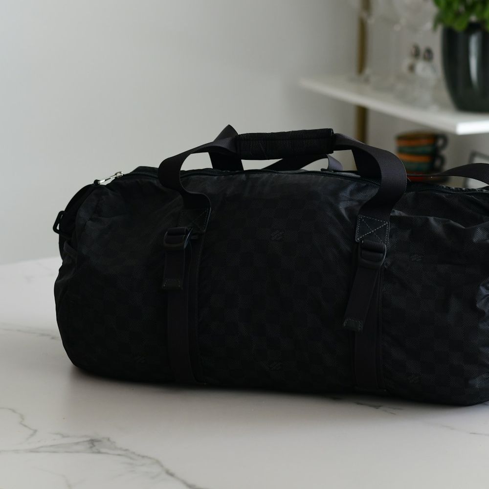 Black barrel-shaped duffel bag with top handles sitting on a white marble table