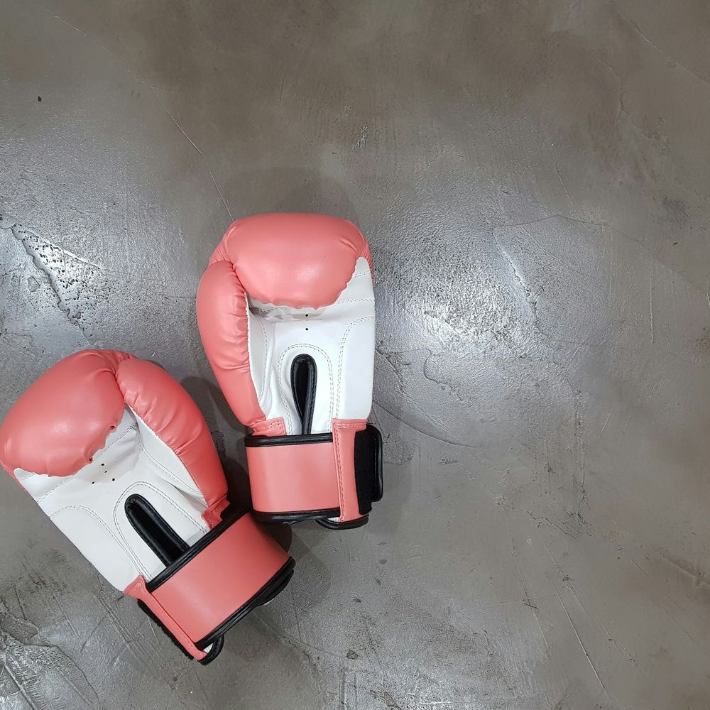 Pair of coral pink and white boxing gloves on a grey concrete floor