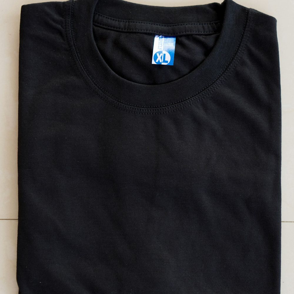 Black crew-neck t-shirt folded flat, photographed from above with the collar and a size label visible