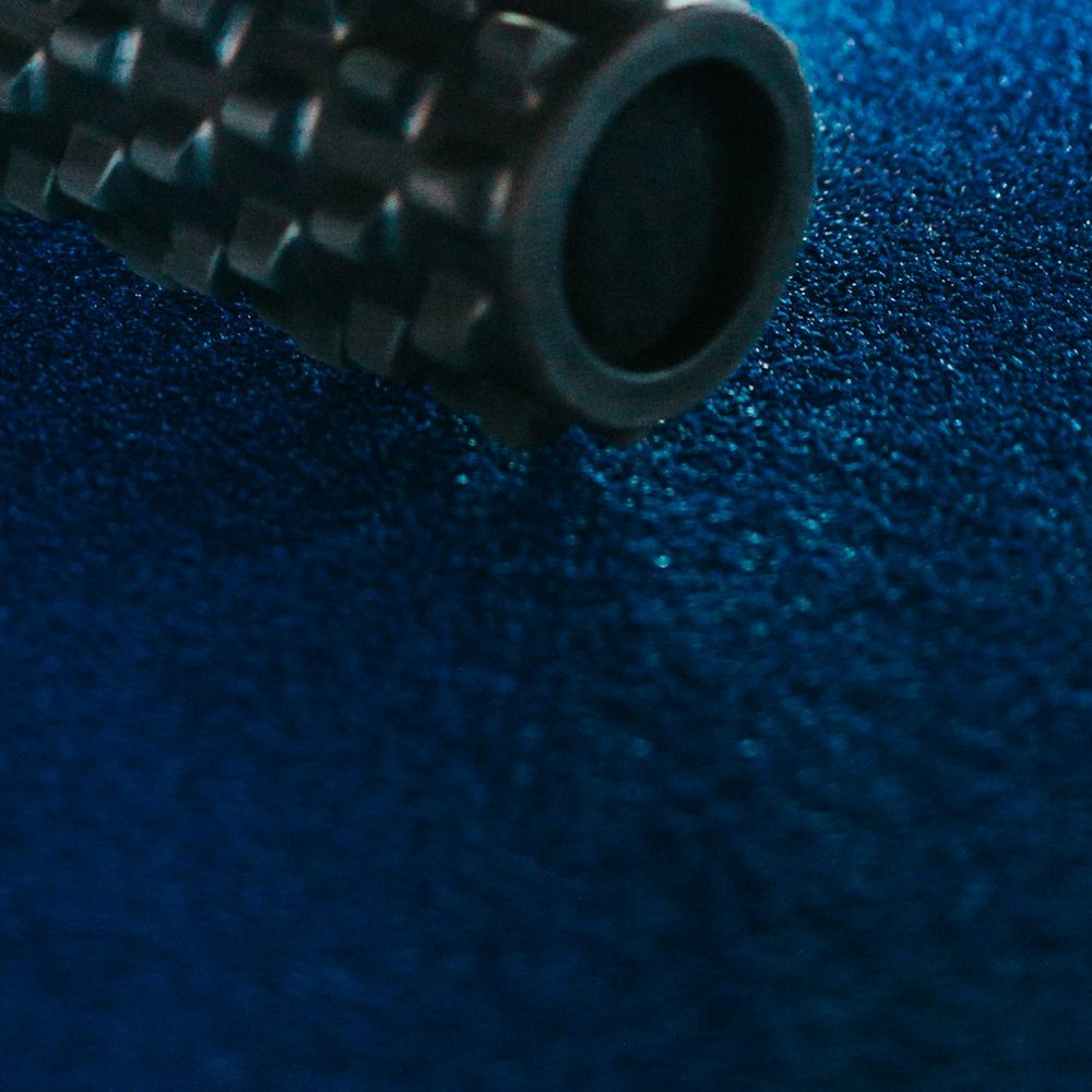 Black foam roller with raised ridges lying on a blue floor